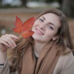 Happy millennial woman with red leaf enjoying autumn in park